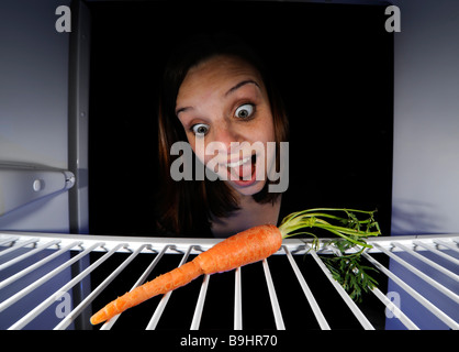 Young woman regarding a single carrot in an empty refrigerator Stock Photo