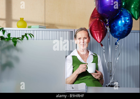 Senior woman with balloons at desk Stock Photo