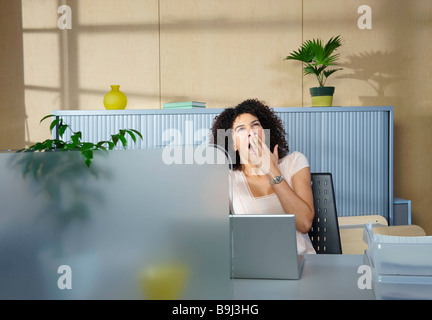 Woman yawning at desk in office Stock Photo