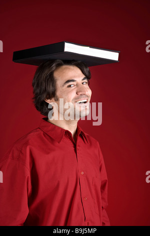 Young, laughing man with a book on his head Stock Photo