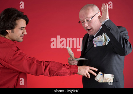 Rich businessman defending himself against a young man, who is trying to pull money from the businessman's pockets Stock Photo