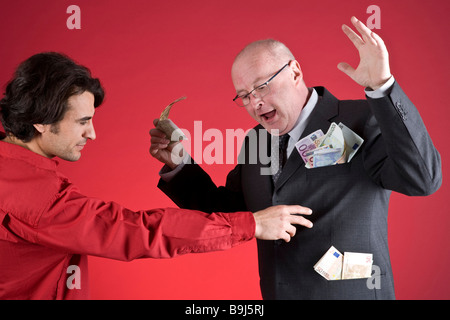 Rich businessman defending himself against a young man, who is trying to pull money from the businessman's pockets Stock Photo