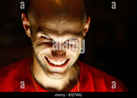 terrifying man with a grin as a smile looking at the camera with his chin down and dramatic light under his face Stock Photo
