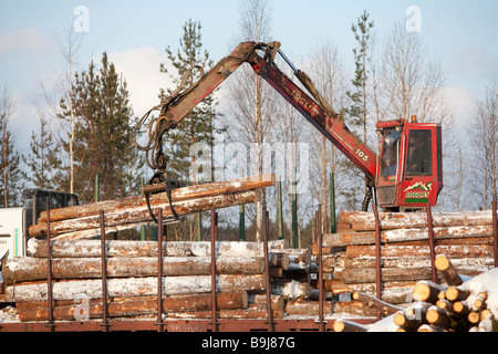 Log truck driver using truck crane and loading logs to cargo log train cars at railroad depot at Winter . Finland Stock Photo