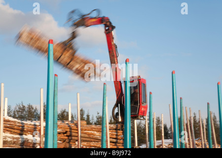 Log truck driver using truck crane and loading logs to cargo log train cars at railroad depot at Winter . Finland Stock Photo