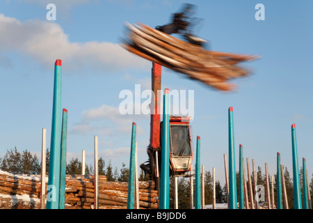 Log truck driver using truck crane and loading logs to cargo log train cars at railroad depot at Winter . Finland Stock Photo