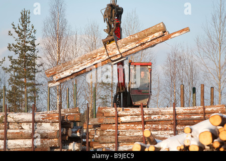 Log truck driver using truck crane and loading logs to cargo log train cars at railroad depot at Winter . Finland Stock Photo