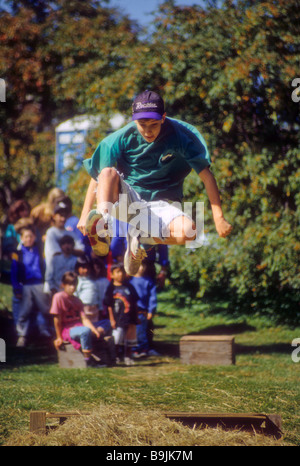 Boy jump barrier hay try high hard leap compete friend fun enjoy fall festival carnival event fair Stock Photo