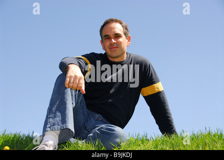 Man sitting outside on a grass on a background of cloudless blue sky Stock Photo
