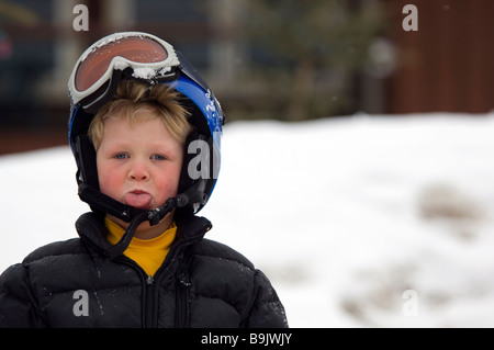 A 4-year-old boy in a ski helmet and goggles sticks his tongue out. Stock Photo