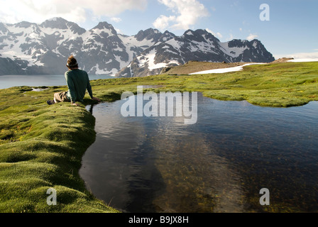 A young man sits next to a small pool enjoying a view of distant snow covered mountains. Stock Photo