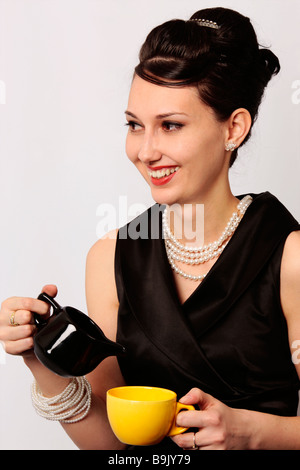 Stylish smiling lady serving tea at breakfast in a classic looking outfit dress isolated on white background Stock Photo