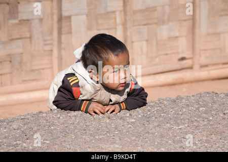 In a small village between Luang Prabang and Phonsavan a baby boy leans against the edge of the road to watch the strangers. Stock Photo