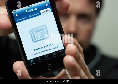 Man holding an Apple iPod Touch that displays the No Friend Requests screen of the Facebook Social Networking Application Stock Photo
