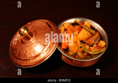 A traditional Indian vegetable curry in an authentic copper-clad serving bowl on a dark wood table. Stock Photo