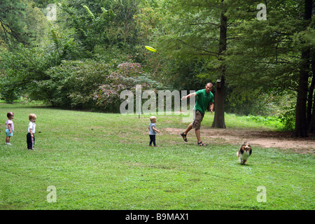 Children watching a young man play frisbee with his dog at the park. Stock Photo