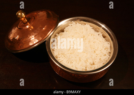 White basmati rice served in an authentic copper-clad Indian serving bowl,on a dark wood table. Stock Photo