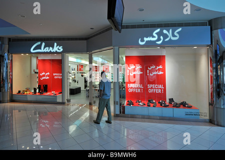 Abu Dhabi Marina shopping Mall shopper outside Clarks shoe shop retail business front window & bilingual sign special offer posters UAE Middle East