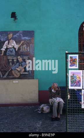 An old man and dog fall asleep next to paintings of tango dancers in La Boca, the artists' quarter of Buenos Aires, Argentina. Stock Photo