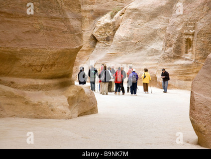 Tourists walking through the siq, past ancient wall carvings, towards the entrance to Petra, Jordan