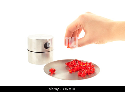 red transparent vitamin pills on a steel round plate hand with one pill white background Stock Photo