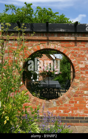 View into a walled garden through circular hole in terracotta brick wall. Stock Photo