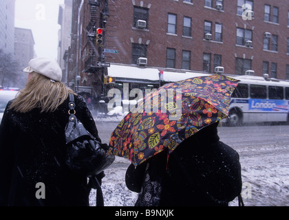 New York City winter weather. People crossing street at bus stop. Street-corner open umbrella. Snow Stock Photo