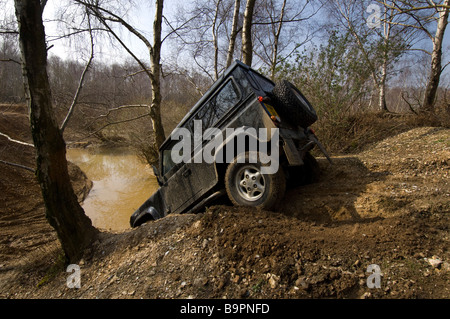 The 2007 design Land Rover Defender 90 creeps down a steep bank to a pond in Slindon West Sussex UK during an Off Road exercise. Stock Photo