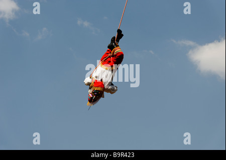 A Mexican Voladore, swiinging upside down during the 'Dance of Papantla's flyers' against a blue sky. Stock Photo