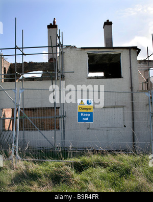 Warning sign attached to fencing outside a burnt out derelict building. It reads ' Danger Keep Out' Stock Photo