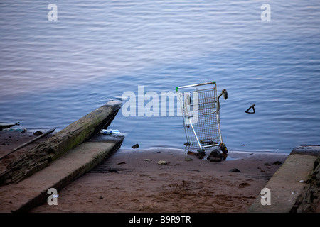 A discarded supermarket trolley lies up-ended at the bottom of a slip-way at the edge of the River Mersey Stock Photo