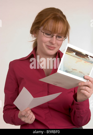 A woman reading a card that has conveyed some happy news that has made her smile Stock Photo