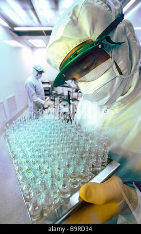 Lab technician wearing sterile suit holding tray of medicine ampules in highly sterile production laboratory. Stock Photo