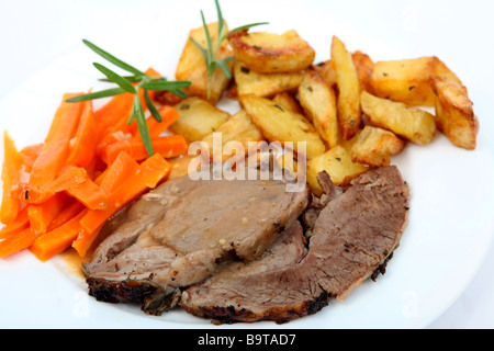 Slices of herbed roast lamb with gravy served with steamed garlic and carrots and diced roast potatoes and sprigs of rosemary