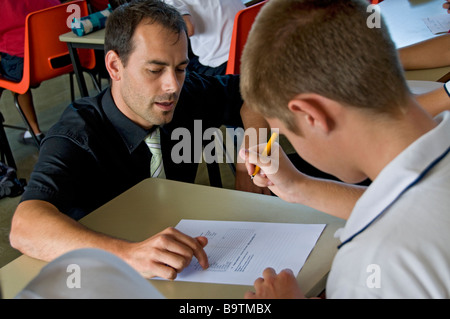 TEACHER PUPIL one to one male teacher coaching teenage boy 15-16 years student pupil in uniform with his work seated at desk in school classroom Stock Photo