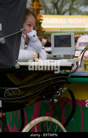 Little Girl in Old Fashioned Pram, watching cartoons on a DVD at the Fun Fair Stock Photo