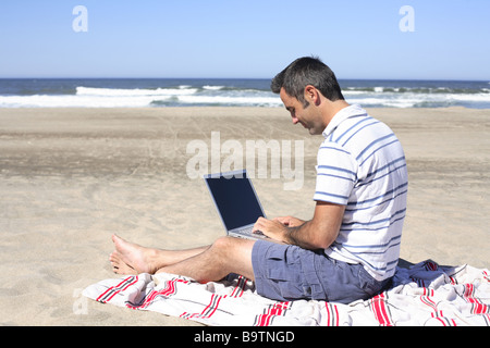 Man using laptop on beach Stock Photo
