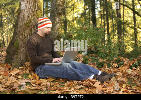Man using laptop outdoors in Fall leaves Stock Photo