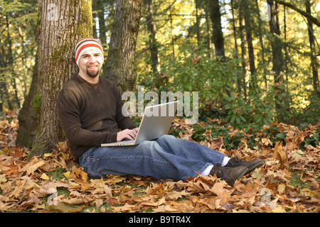 Man using laptop outdoors in Fall leaves Stock Photo
