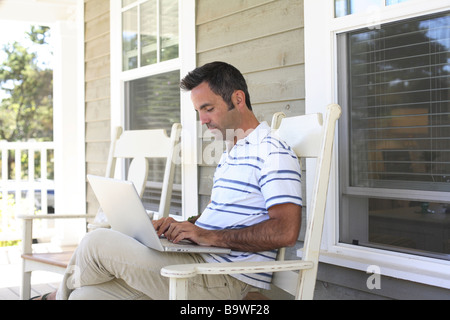 Man sitting on porch with laptop Stock Photo