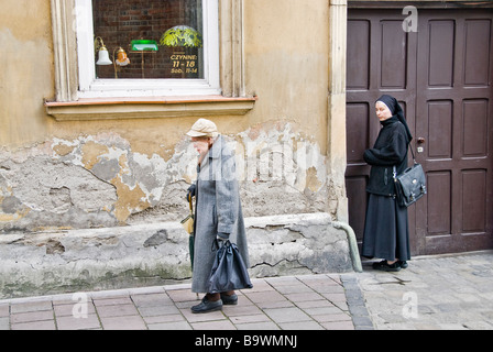 Nun looking at a woman with hat and umbrella walking in the streets of the old city of Krakow, Poland, Europe. Stock Photo