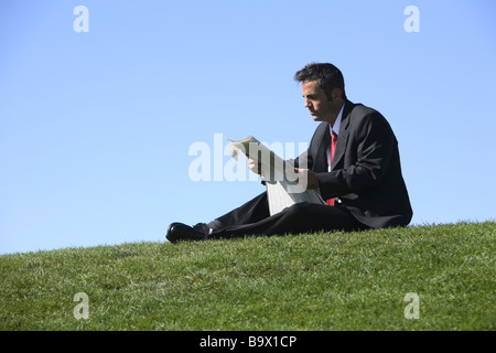 Businessman sitting outdoors with newspaper Stock Photo
