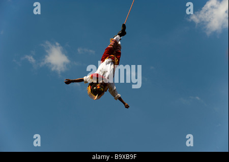 A Mexican Voladore, swiinging upside down during the 'Dance of Papantla's flyers' against a blue sky. Stock Photo