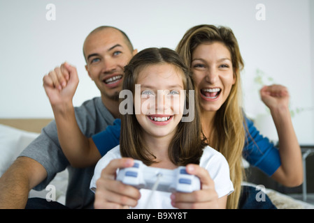 Girl playing video game, parents watching and cheering Stock Photo