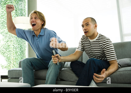 Two men watching TV and cheering on sofa Stock Photo