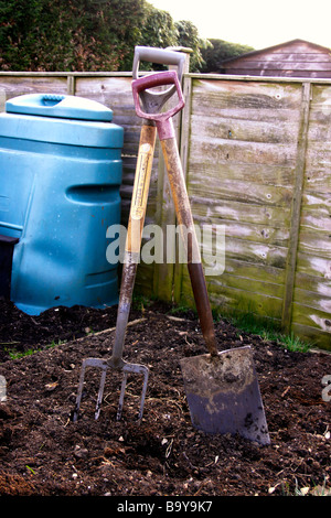 GARDEN TOOLS ON FRESHLY DUG SOIL WITH A HOME COMPOST BIN BEHIND. Stock Photo