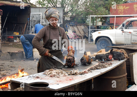 A woman, working at a roadside table, prepares the delicacy of roasted sheep heads, Langa Township, Cape Town, South Africa Stock Photo