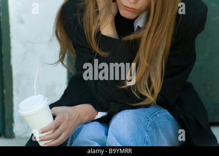 Young woman leaning on elbow, holding cup, cropped view Stock Photo