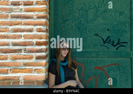 Young woman in sunglasses leaning against wall Stock Photo