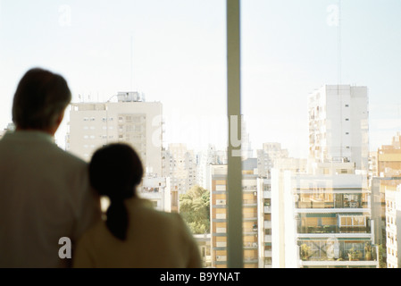 Couple, woman's head on man's shoulder, together at window looking at view of city Stock Photo